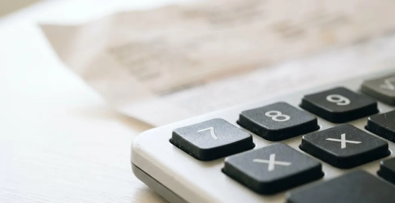 Gros plan en macro sur les touches d'une calculatrice moderne au premier plan avec un devis dentaire papier flouté en arrière-plan sur un bureau blanc